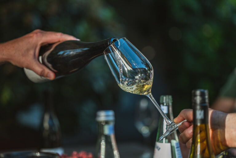 Eine Hand schenkt Weißwein in ein Glas, das von einer anderen Hand gehalten wird.